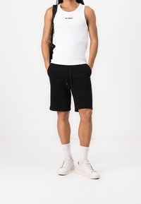 White tank top with black logo, paired with black shorts. Light-colored sneakers and white socks complete the outfit. Simple, casual design.