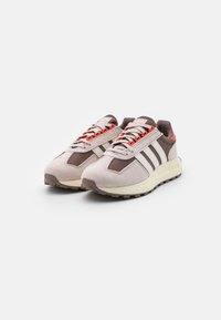 Ljusrosa och bruna sneakers med mesh- och mockamaterial, med tre vita ränder, orange snören och en texturerad gummisula.