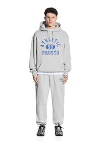 Szara bawełniana bluza z kapturem z grafiką "ATHLETIC 99 PROSTO" w kolorze niebieskim, połączona z dopasowanymi spodniami dresowymi z małym logo. Uzupełniona czarnymi sneakersami.