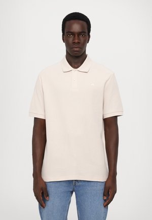 Beige polo shirt with a soft texture, short sleeves, and a three-button placket. Features a small white logo on the chest.