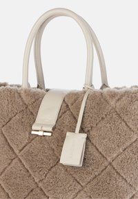 Beige quilted handbag made of soft fabric with leather handles and a detachable tag; features a smooth texture and gold hardware accents.