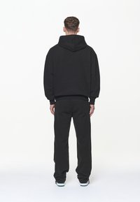 Sort hættetrøje med afslappet pasform og stor hætte, kombineret med sorte bukser med vide ben. Materialet virker blødt og glat, med minimale detaljer.