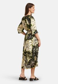 Langes Kleid mit floralem Blattmuster in Grün, Schwarz und Creme. Verfügt über einen Taillengürtel und weite Ärmeln, gefertigt aus leichtem Stoff.