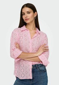 Camicia rosa in pizzo con motivo a fiori ritagliato, dotata di colletto, chiusura con bottoni e maniche arrotolate.