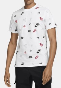 T-shirt bianca in cotone con vari loghi Nike in rosso, nero e grigio. Maniche corte e design a girocollo.