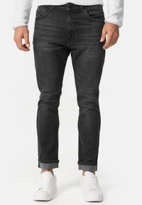 Jeans de mezclilla oscuros con un ajuste slim, diseño de cinco bolsillos y bajos enrollados, combinados con zapatillas blancas. La tela parece suave y con un desgaste mínimo.