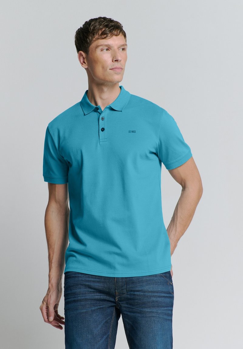 Turquoise polo shirt met een klassieke kraag, korte mouwen, een drie-knoopsluiting en een klein logo op de borst, gedragen met blauwe jeans.