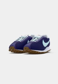 Par de ténis Nike em malha azul-marinho com swooshes azul-claro, atacadores brancos, entressolas brancas e solados de borracha de gengibre, lado a lado em fundo branco.