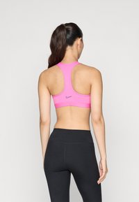 Roze sportbeha met een racerback-ontwerp, gemaakt van rekbare stof. Nike-logo in een donkere kleur op de rug. Zwarte high-waisted leggings.