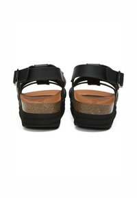 Black sandals with adjustable straps, cork footbed, and textured sole. The design features a flat heel and minimalistic back.