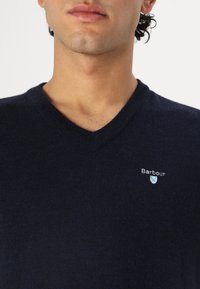 Navyblaue V-Neck-Pullover aus weichem Material, mit kleinem gesticktem Barbour-Logo auf der Brust und glatter Textur.