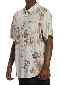 Lyhythihainen paita, joka on tehty kevyestä kankaasta ja jossa on kukkakuosi purppuran, keltaisen ja vaaleanpunaisen sävyissä kermanvärisellä pohjalla sekä rintatasku.