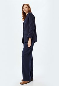 Marineblazer en bijpassende wijde broek van zachte stof, met een comfortabele pasvorm en minimalistisch ontwerp met subtiele zakdetails.