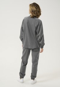 Gray textured two-piece outfit featuring a loose-fitting, long-sleeve top and tapered pants with elastic cuffs and matching white sneakers.