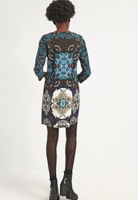 Färgguldig klänning med ett lapptäcksmönster i blommor och leopardmönster. Tillverkad av tyg, långa ärmar och en figurnära passform. Svarta ankelskor.