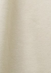 Tissu tricoté beige avec une texture fine et régulière ainsi que des variations subtiles de nuances suggérant un matériau doux.