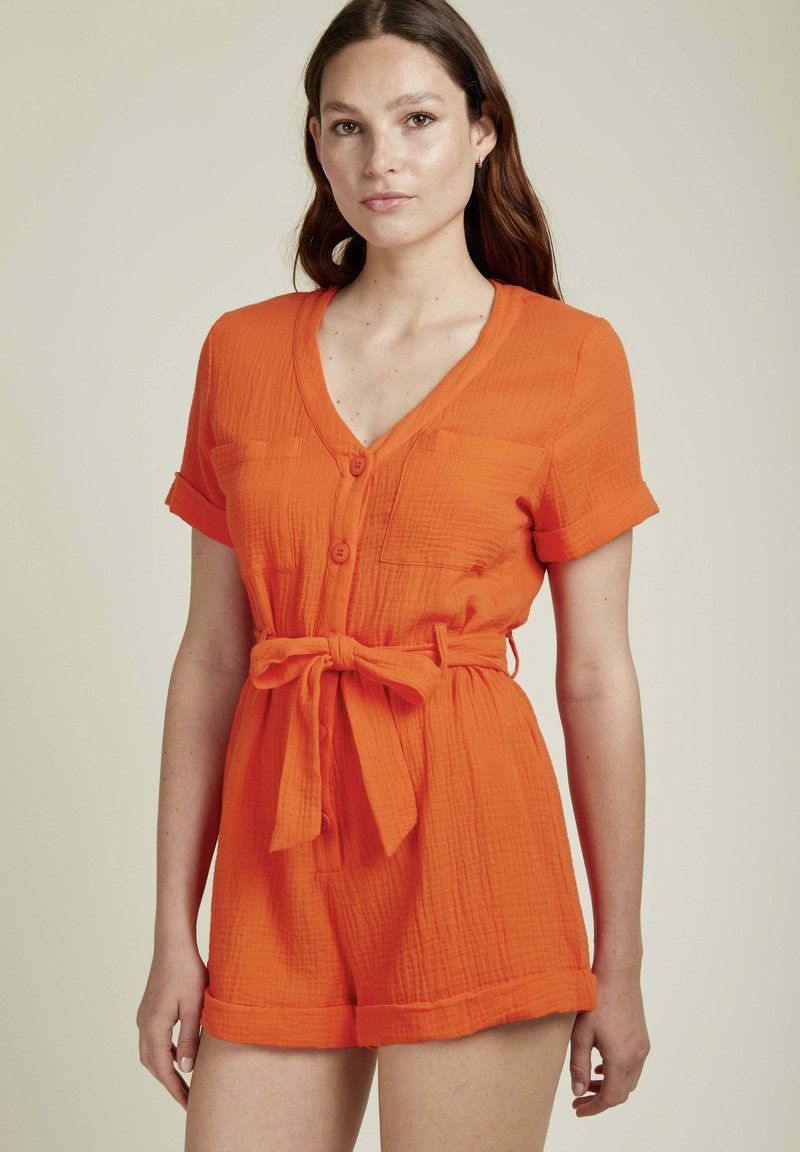 Robe-pantalon orange à manches courtes, avec un col en V et une taille nouée. Dispose de deux poches avant et d'un tissu texturé.