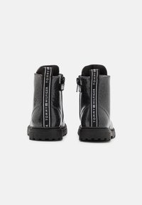 Botas de tobillo de charol negro con un acabado brillante, que cuentan con una cremallera trasera y el logo de Tommy Hilfiger en los lados. Suela de goma texturizada.