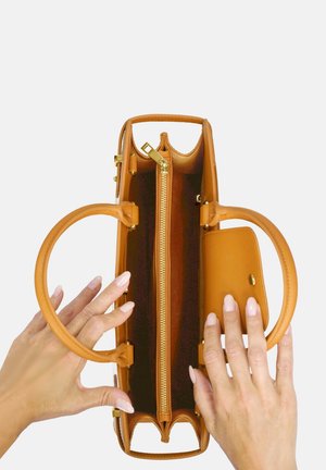 Sac à main en cuir tan avec des poignées rondes, compartiment zippé et une petite poche à l'avant. L'intérieur présente une doublure texturée et des finitions dorées.