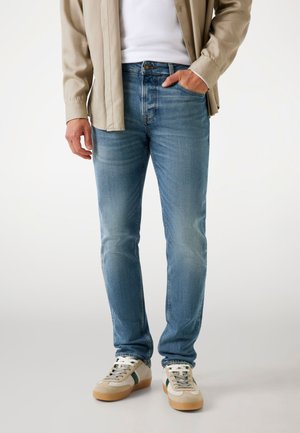 Light blue denim jeans with a straight fit, faded texture, and classic five-pocket design. Paired with beige shoes and a light top.
