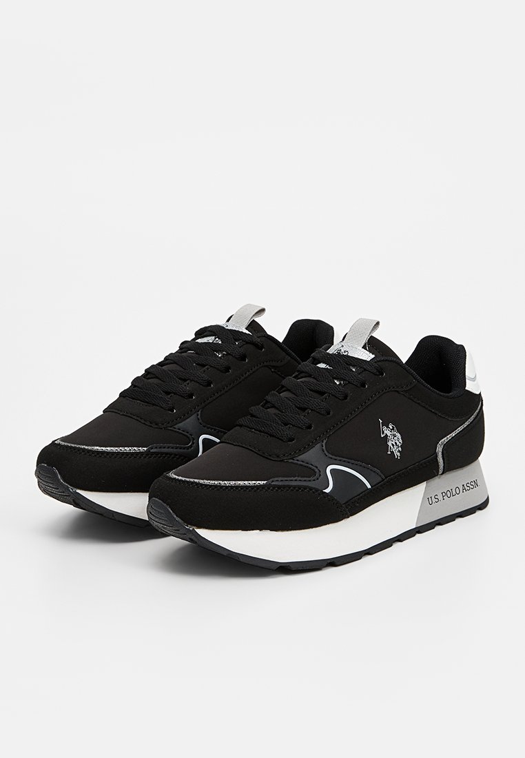 Zapatillas negras con parte superior de tela texturizada, acentos brillantes y suela de goma blanca. Presentan un diseño de cordones y un logo en el lateral.