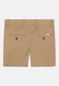 Tan shorts lavet af glat stof, med to baglommer med runde brune knapper og et lille brandmærke på højre side.