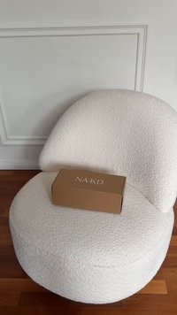 Kreemikas toon, tekstuuriga ümmargune tool pehme pinnaga ja selle peal paiknev pruun ristkülikukujuline karp, millel on silt "NA-KD".