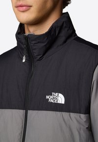 Gevoerde jas in zwart en grijs, met een hoge kraag, frontale rits en het logo van The North Face in het wit op de borst. Lichtgewicht materiaal.