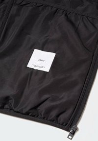 Schwarze Nylonjacke mit einem Innenfutter und einem Etikett mit der Aufschrift "MNG." Verfügt über eine glatte Textur, elastisches Bündchen am Saum und ein seitliches Reißverschlussdetail.