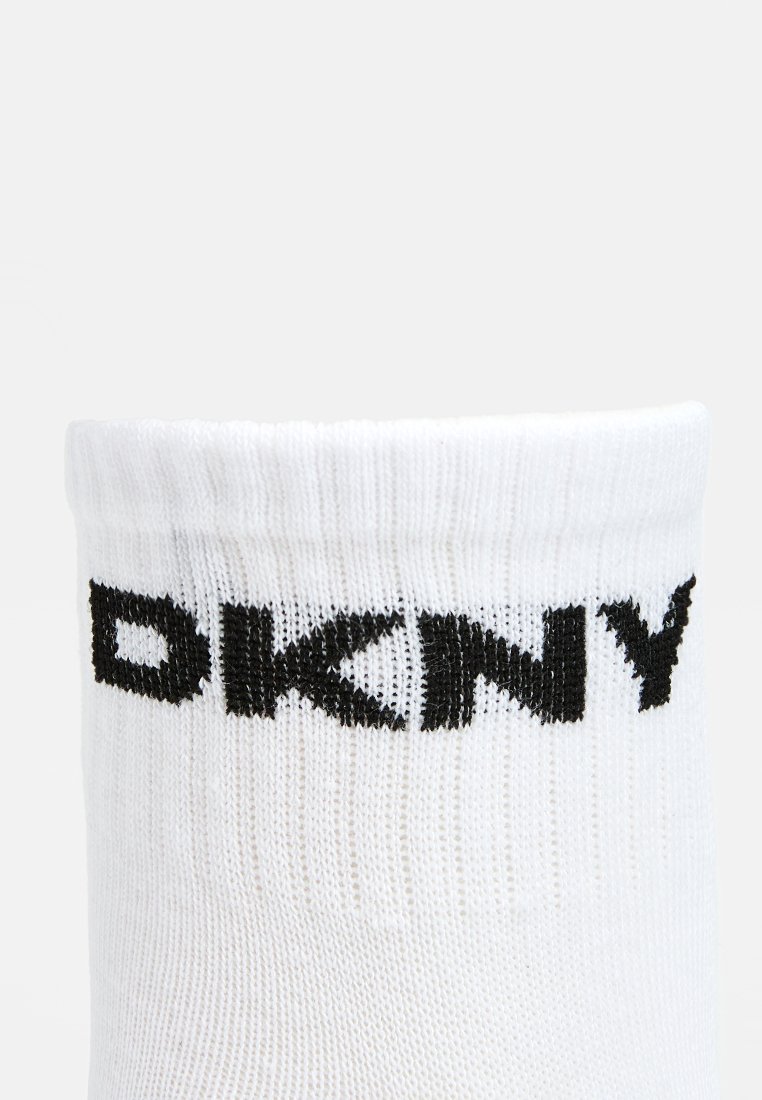 Weiße Baumwollsocke mit geripptem Textur, die das schwarze "DKNY"-Logo nahe der Oberkante deutlich zeigt. Einfaches Design, keine anderen Muster oder Akzente.