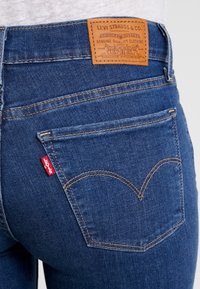 Mörkblå denimjeans med en medelhög passform, med en läderlapp vid midjan, rundade bakfickor och en röd logotypflik på sidan.