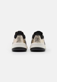 Černé a kovově zlaté tenisky s texturovaným svrškem, bílou střední podešví a černou gumovou podrážkou. Mají poutko na patě pro snadné nazouvání.