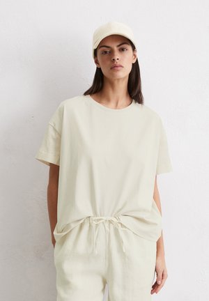 T-shirt crème à manches courtes avec une coupe décontractée, associé à un pantalon à cordon de serrage assorti. Tissu lisse et léger avec un design minimaliste.