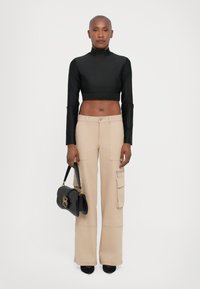 Zwarte cropped top met lange mouwen en een gestructureerde tailleband, gecombineerd met beige wijde cargobroek met zakken. Bevat een kleine zwarte handtas.
