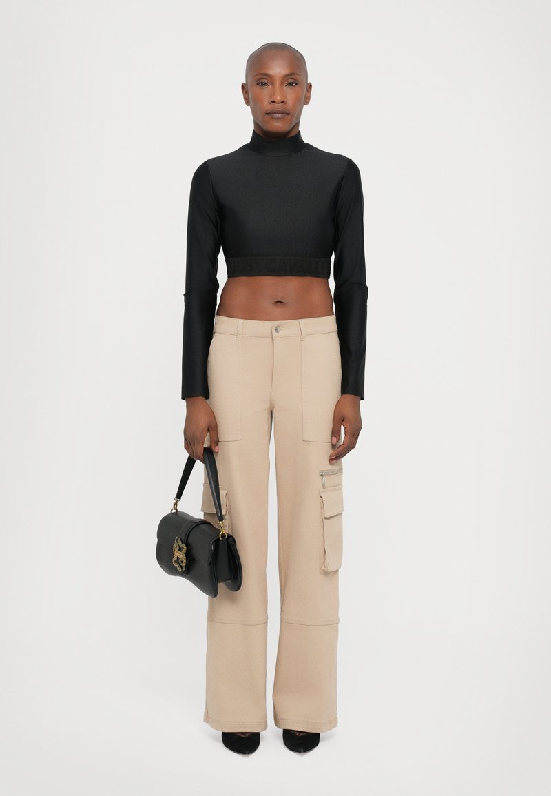 Zwarte cropped top met lange mouwen en een gestructureerde tailleband, gecombineerd met beige wijde cargobroek met zakken. Bevat een kleine zwarte handtas.
