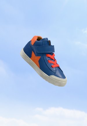 Baskets pour enfants bleu et orange avec bride en Velcro, motif étoile et lacets orange vif sur fond de ciel bleu clair.