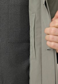 Material exterior de culoare gri deschis, cu o textură netedă, care dezvăluie o căptușeală interioară de culoare gri închis, având detalii de buzunar, evidențiind un design stratificat.