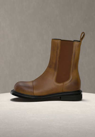 Bottine Chelsea en cuir marron avec panneaux latéraux élastiques, semelle noire et languette de traction, présentée sur une surface claire avec un fond uni.