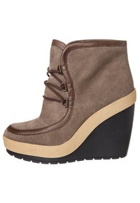 Stivale alla caviglia in suede marrone con tacco a zeppa e suola in gomma color crema. Presenta lacci decorativi e punta arrotondata. Dettagli in pelle liscia lungo la parte superiore.