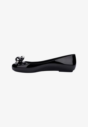 Ballerine en cuir verni noir avec un bout arrondi, dotée d'un petit nœud décoratif avec un accent métallique sur le bout. Texture lisse.