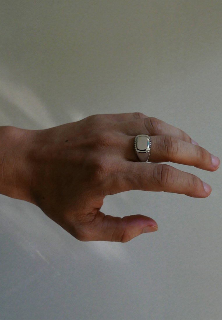 Anello in argento con un centro rettangolare liscio, caratterizzato da una fascia scanalata e una finitura lucida. Mano posizionata con le dita leggermente divaricate.