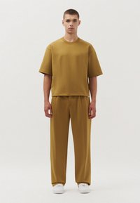 Mosterdgele gebreide t-shirt met korte mouwen en een rechte snit, gecombineerd met bijpassende brede broek. Witte sneakers maken de outfit compleet.