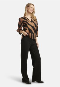 Blusa a righe marroni e nere con scollatura a V, maniche a tre quarti, abbinata a pantaloni neri a gamba larga e scarpe nere. Tessuto morbido.