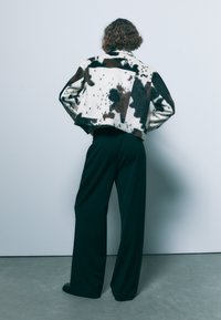 Kratka jakna iz umetnega krzna z vzorcem črno-belega kravjega reljefa. Usklajena z širokimi črnimi hlačami. Zadnji pogled.