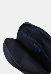 Borsa in tessuto nero con apertura con zip, dotata di scomparti interni e un'etichetta con il marchio, progettata per l'organizzazione e lo stoccaggio.