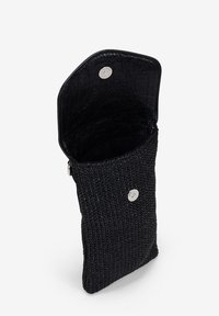 Bolso de mano negro tejido con un acabado texturizado, parte superior abierta y cierre de presión con un acento plateado. El interior es forrado y suave.