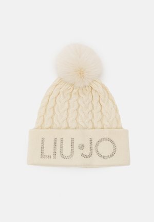 Cappello di maglia a trecce color crema con pompon soffice sulla parte superiore e risvolto che presenta un embellimento con logo di strass argentati.