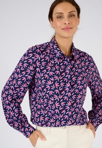 Blusa a maniche lunghe blu navy con un motivo floreale in rosa e blu. Presenta un colletto e una chiusura frontale con bottoni; tessuto morbido.