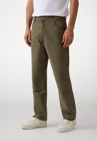 Khaki katoenen cargo broek met een relaxed fit, voorzien van zijzakken, kniestukken en subtiele stikdetails. Draagt met witte sneakers.