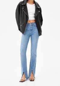 Svart konstläder oversized jacka, vit åtsittande croppad topp, ljusblå utsvängda jeans med främre slitsar, och svarta sandaler med remmar.